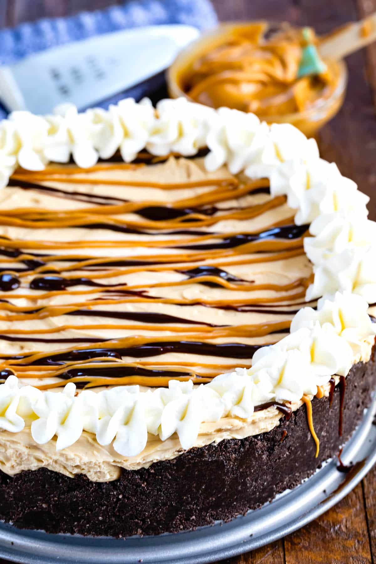 cheesecake with peanut butter and chocolate sauce drizzled over it and whipped cream on the edge.