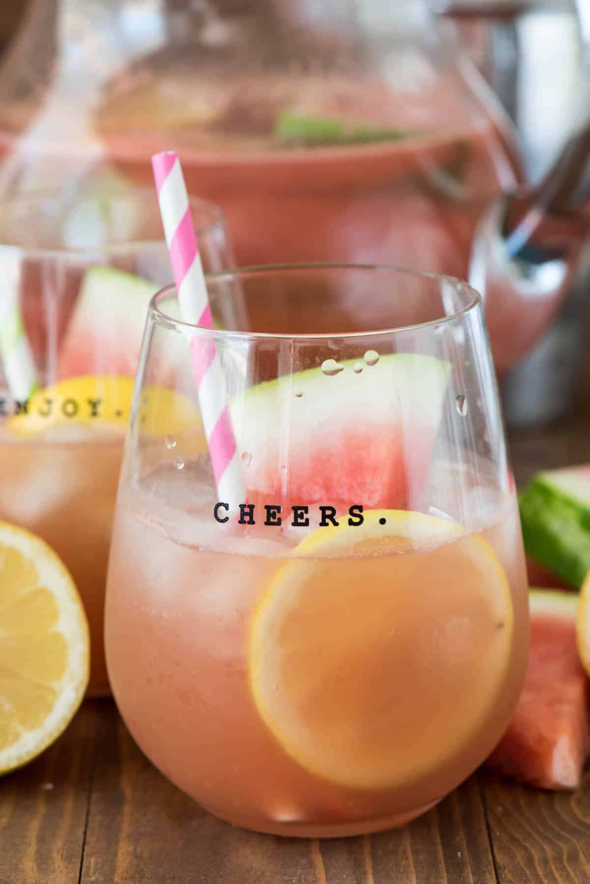 margarita in a short clear glass with sliced watermelons and lemons and a pink and white straw.