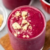 pink smoothie in a clear glass with crumbled cookies on top.