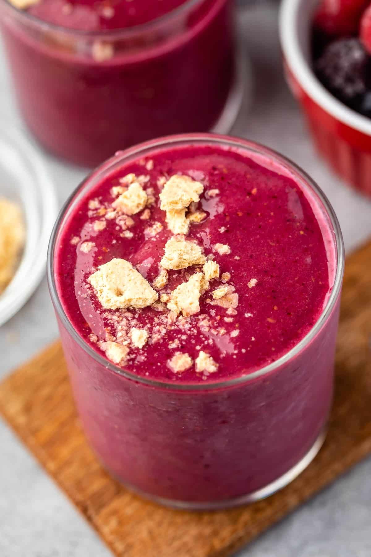 pink smoothie in a clear glass with crumbled cookies on top.