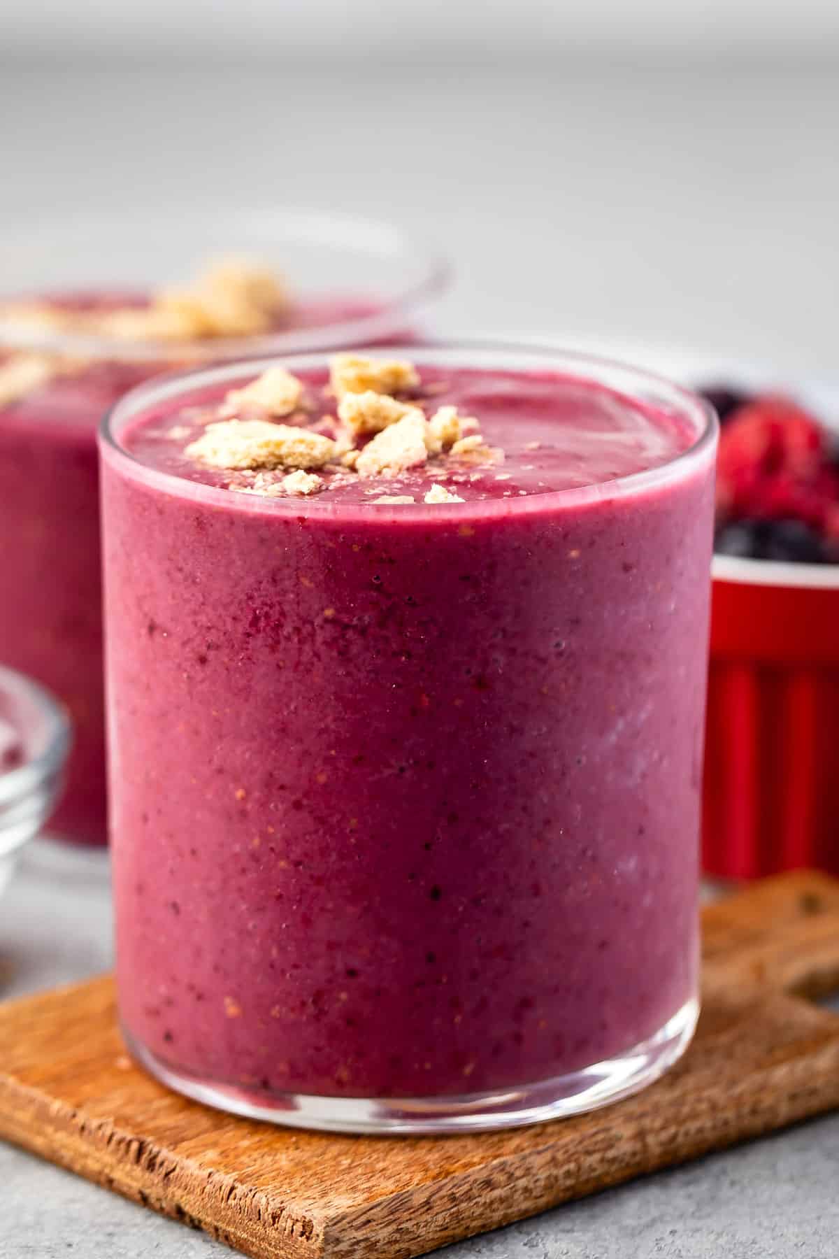 pink smoothie in a clear glass with crumbled cookies on top.
