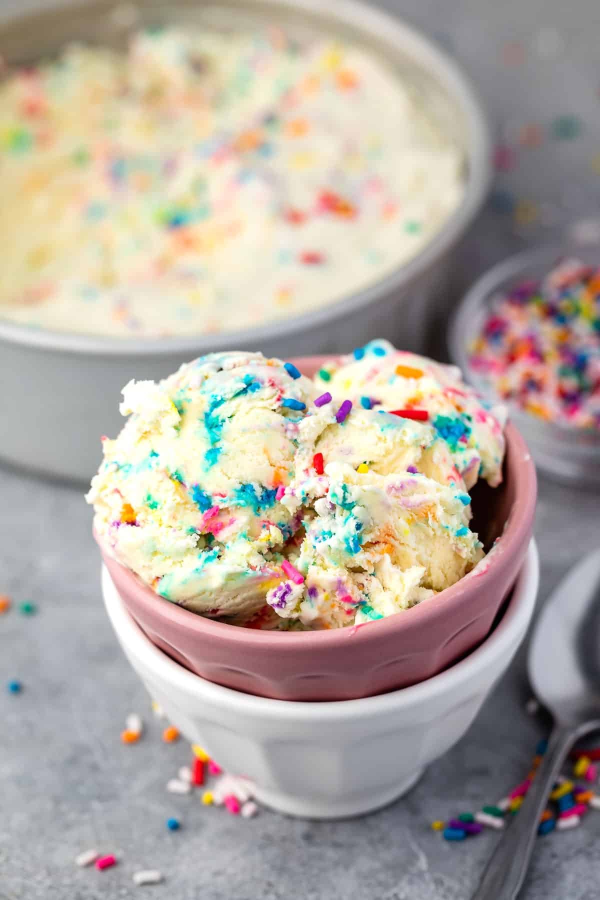 scooped ice cream with sprinkles mixed in, in pink and white stacked bowls.