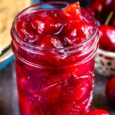 cherry pie in a clear mason jar surrounded by cherries.