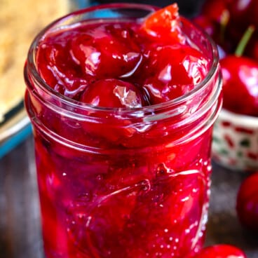 cherry pie in a clear mason jar surrounded by cherries.
