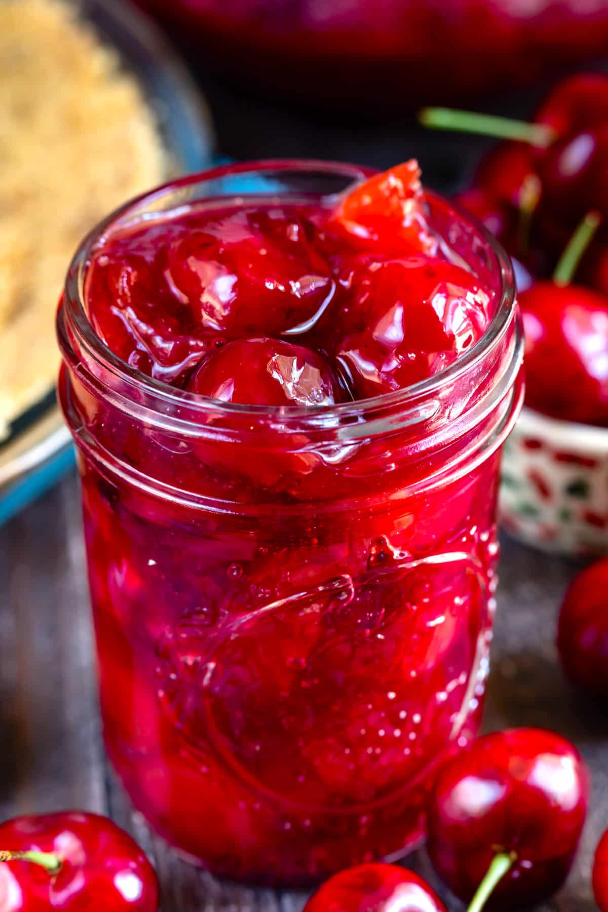 cherry pie in a clear mason jar surrounded by cherries.