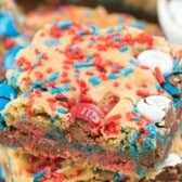 A close-up of festive blondies topped with red, white, and blue M&M candies and colorful sprinkles. These dessert bars boast a chewy, cookie-like texture that's perfect for celebrations.