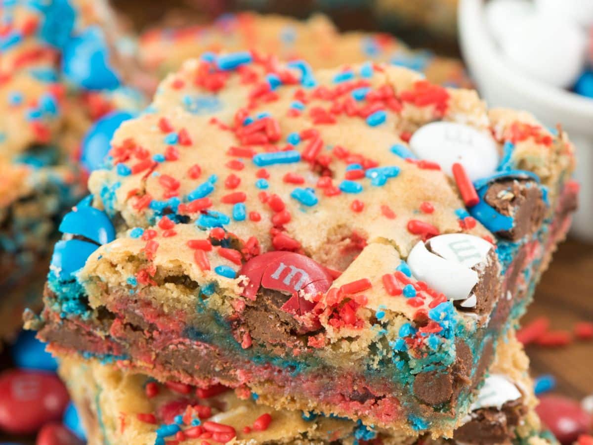 A close-up of festive blondies topped with red, white, and blue M&M candies and colorful sprinkles. These dessert bars boast a chewy, cookie-like texture that's perfect for celebrations.