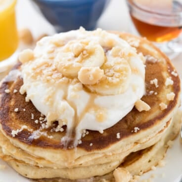 stacked pancakes on a white plate with banana slices on top.