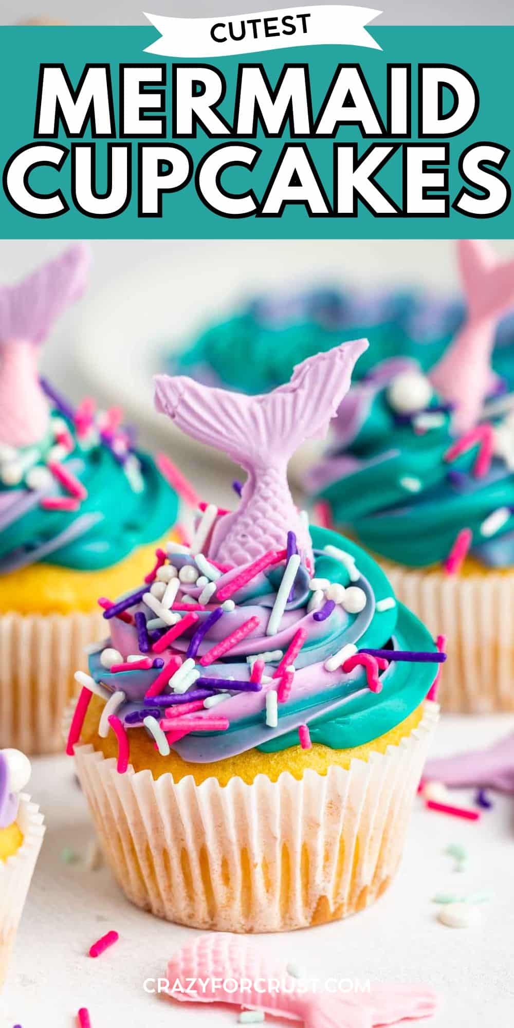 A colorful mermaid cupcake topped with blue and purple swirled frosting, sprinkles, and a purple chocolate mermaid tail decoration. Other mermaid cupcakes are blurred in the background. Text reads Cutest Mermaid Cupcakes.