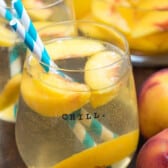 glass of sangria with peaches and striped straws.