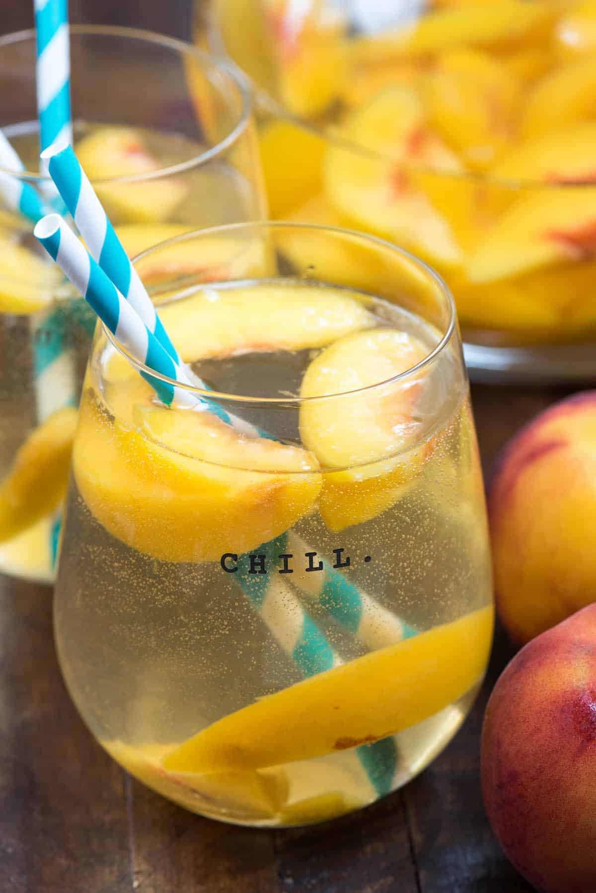 glass of sangria with peaches and striped straws.