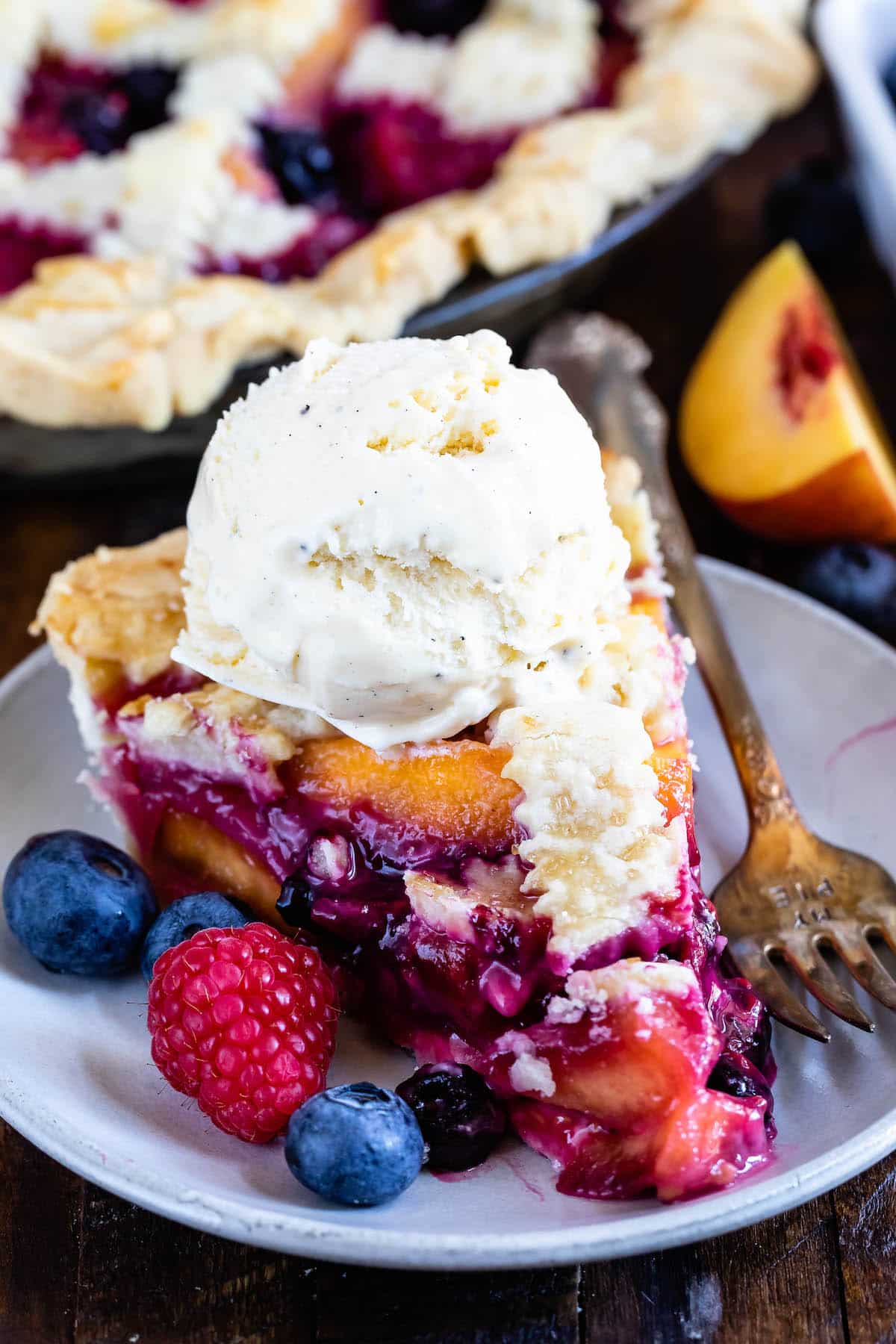 berry pie with decorative pie crust on top surrounded by slice fruit with ice cream on top.
