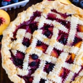 berry pie with decorative pie crust on top surrounded by slice fruit.
