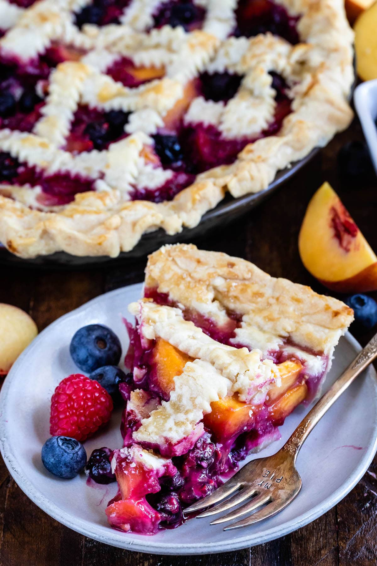 berry pie with decorative pie crust on top surrounded by slice fruit.