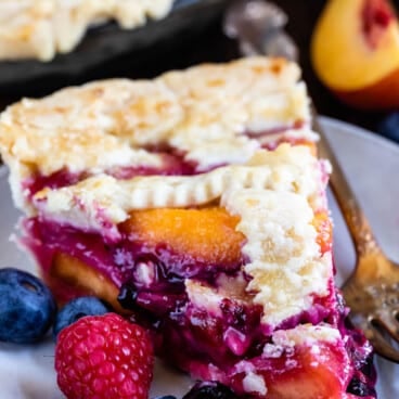 berry pie with decorative pie crust on top surrounded by slice fruit.