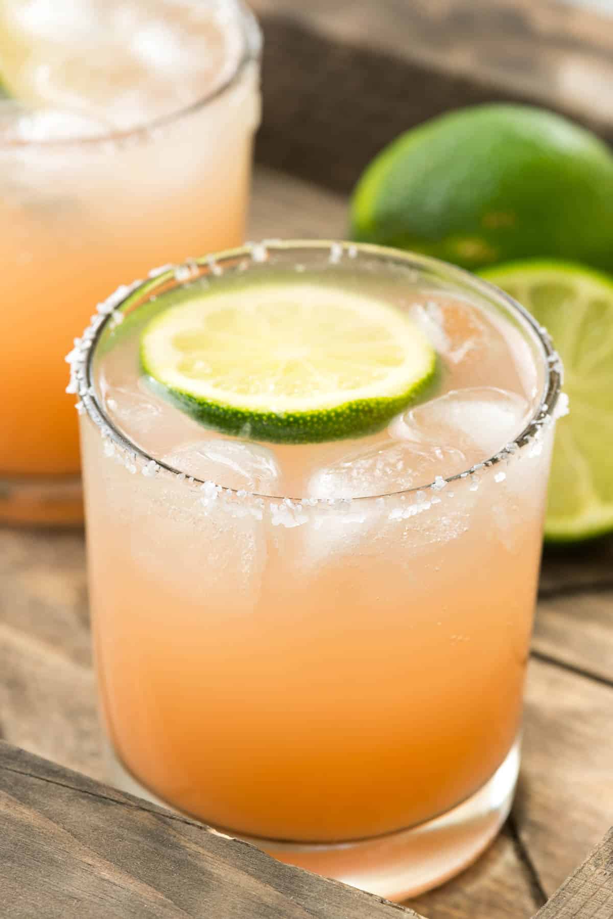 peach colored drink in a short clear glass with a lime slice in the drink.