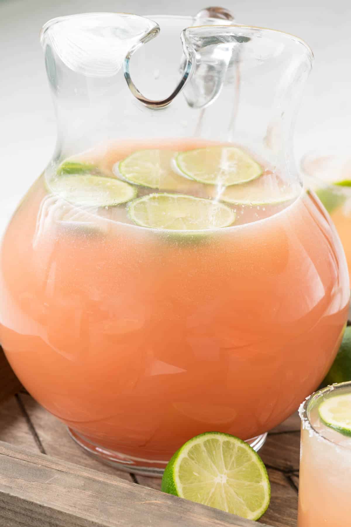 peach colored drink in a glass pitcher with a lime slice in the drink.