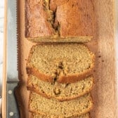 sliced banana bread next to a serrated knife on a cutting board.