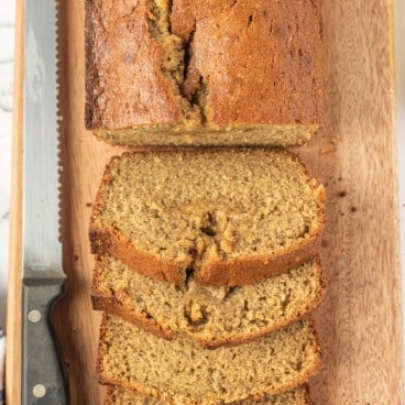 sliced banana bread next to a serrated knife on a cutting board.