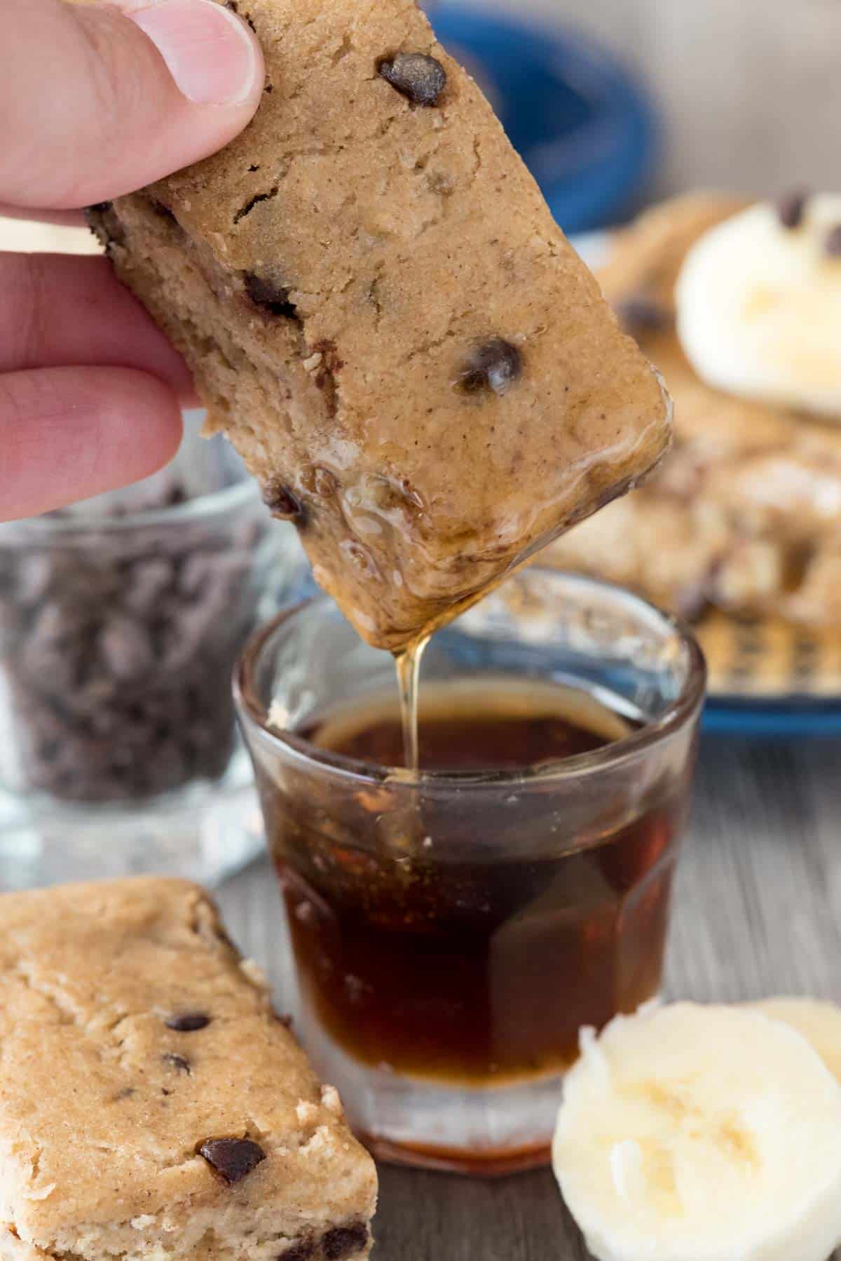 hand holding pancake that's being dipped in syrup.