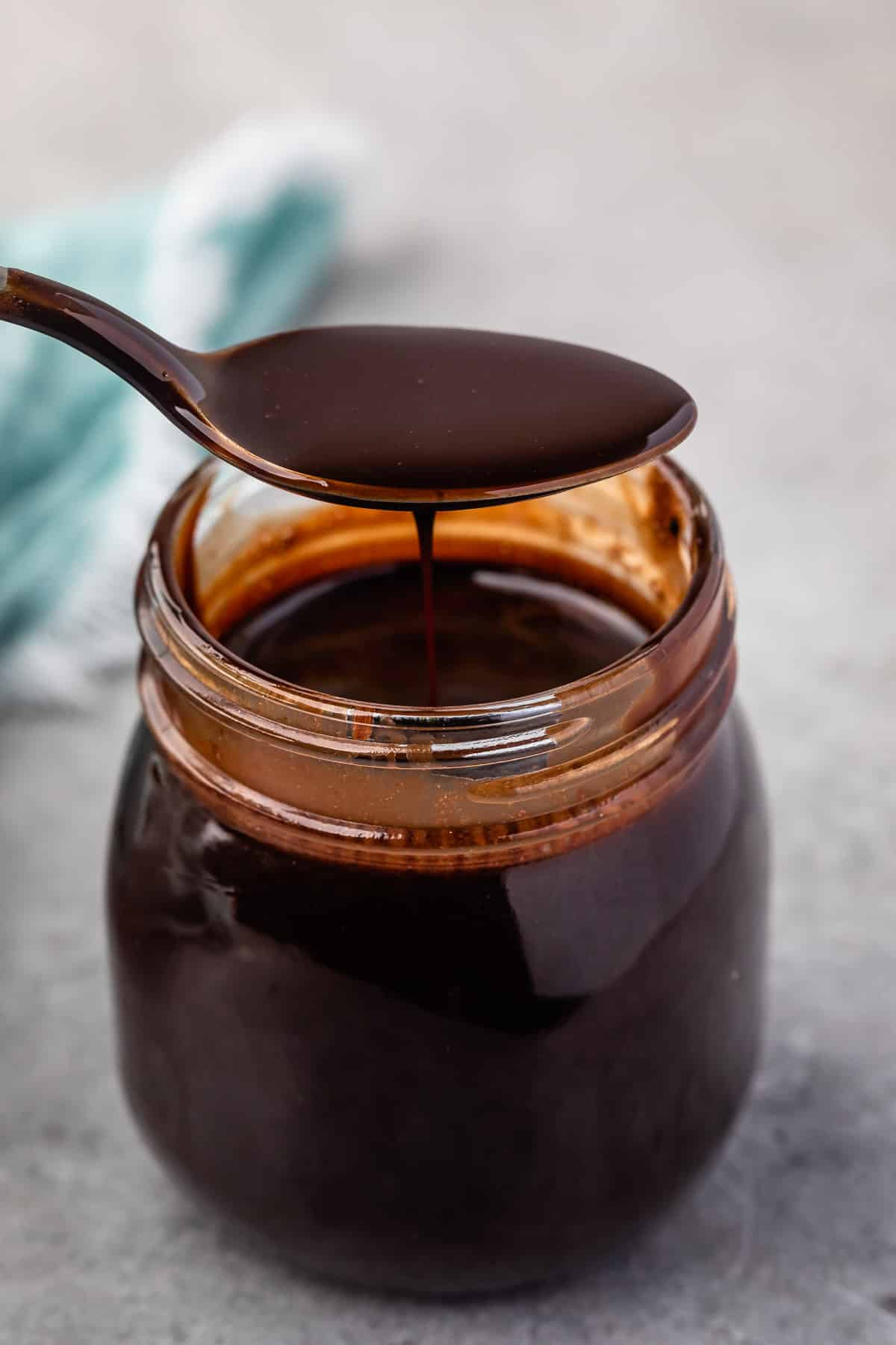 a spoon scooping chocolate sauce out of a clear jar.