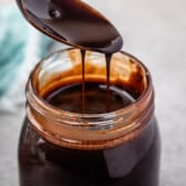 a spoon scooping chocolate sauce out of a clear jar.