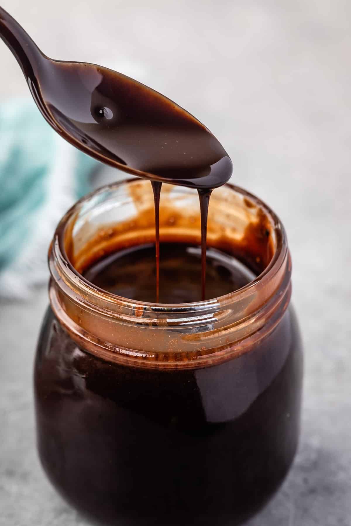 a spoon scooping chocolate sauce out of a clear jar.