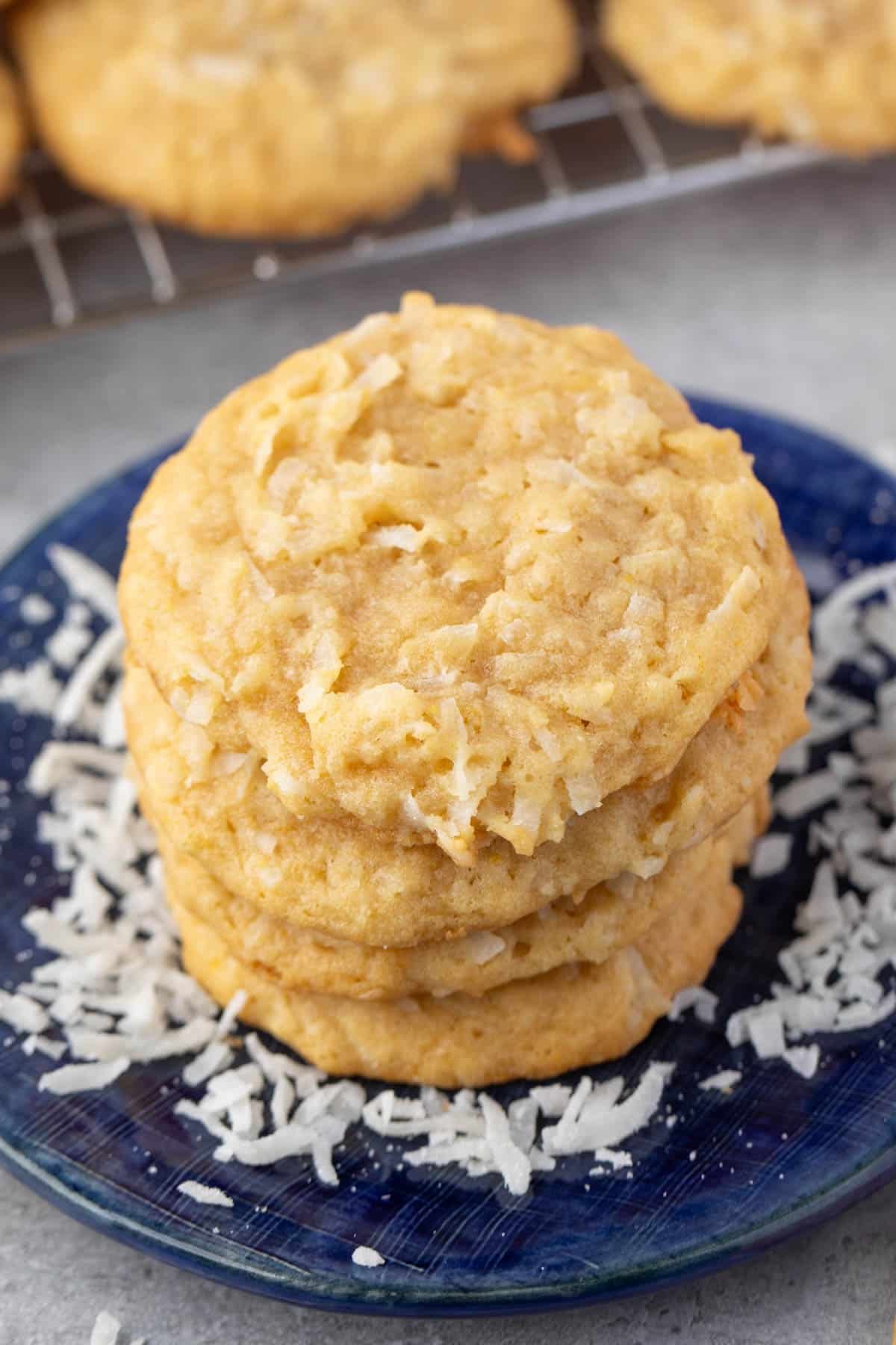 stacked coconut cookies on a navy blue plate with sprinkles coconut around the cookies.