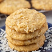 stacked coconut cookies on a navy blue plate with sprinkles coconut around the cookies.