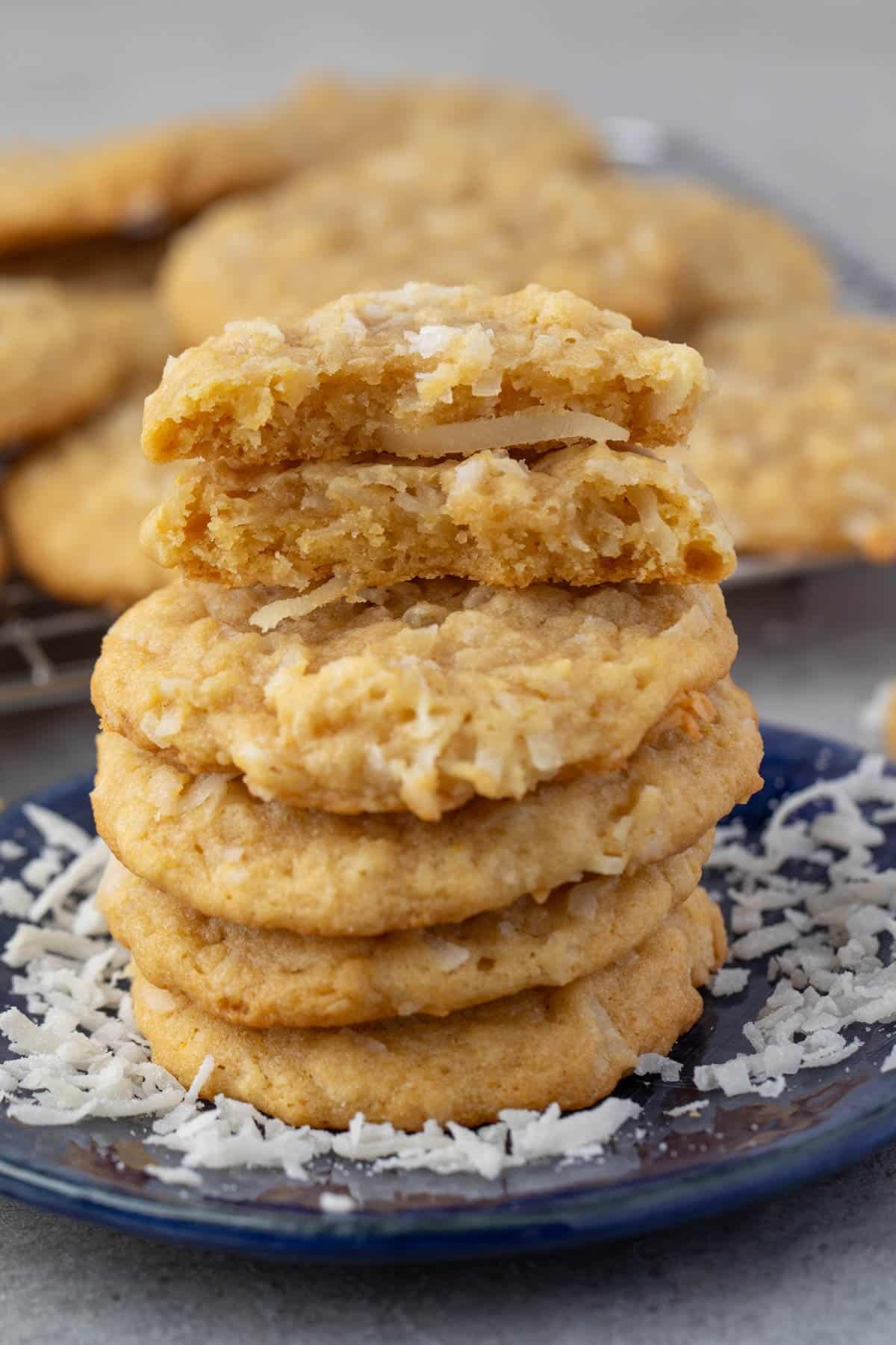 stacked coconut cookies on a navy blue plate with sprinkles coconut around the cookies.