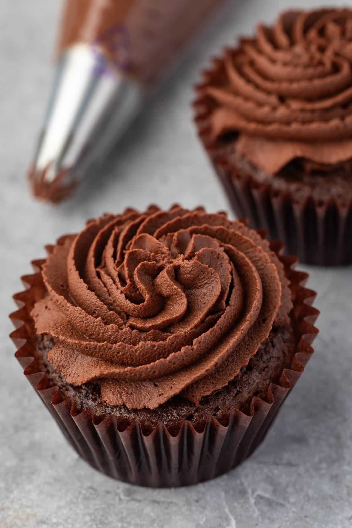 ganache on top of a chocolate cupcake in brown cupcake wrappers.