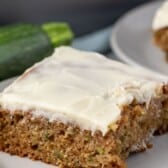 square slice of zucchini cake on a grey plate next to a fork with words on the image.