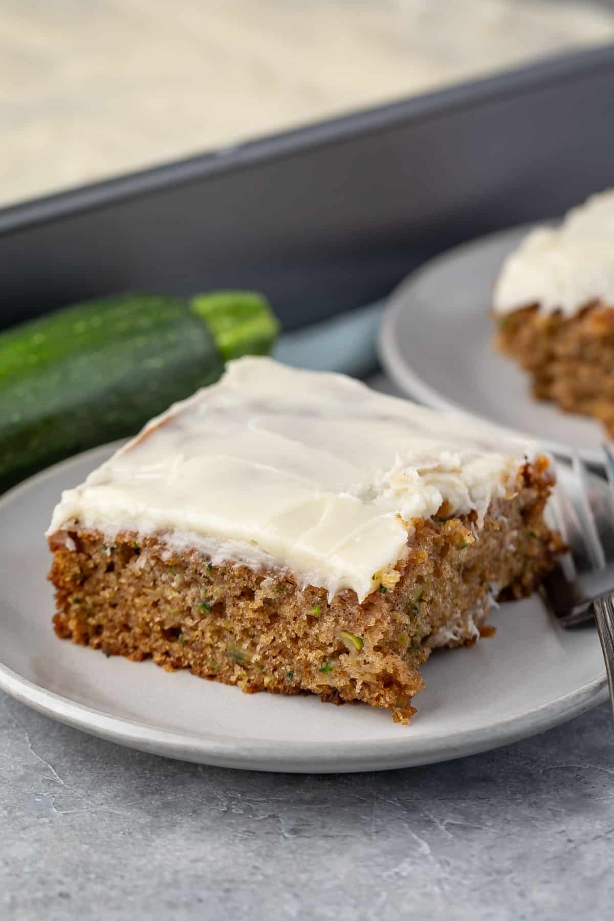 square slice of zucchini cake on a grey plate next to a fork.