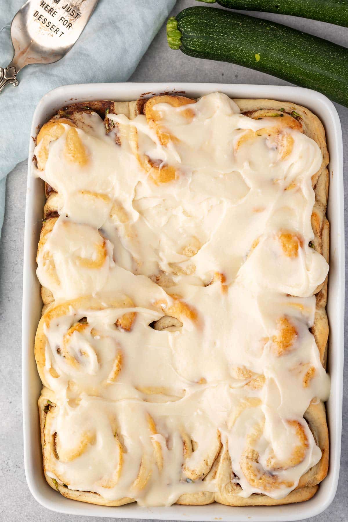 zucchini cinnamon rolls in a white pan covered in frosting.