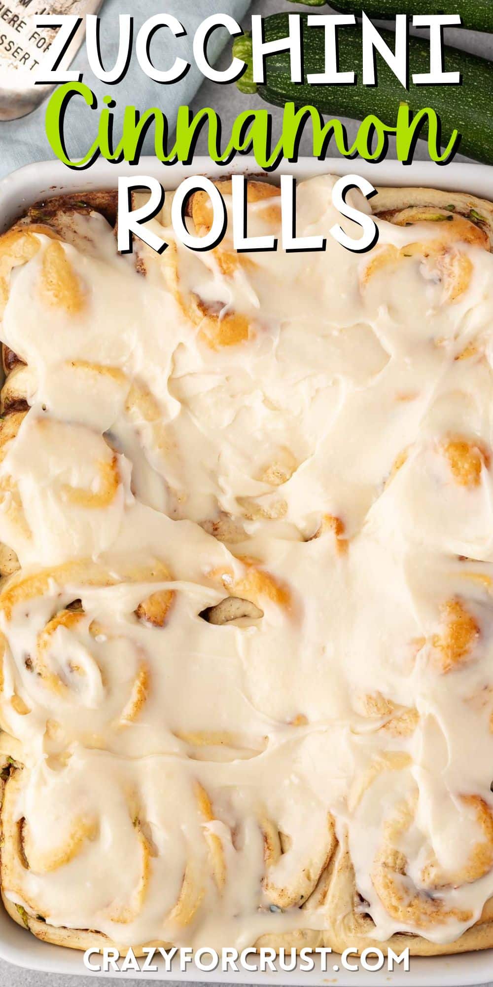 zucchini cinnamon rolls in a white pan covered in frosting with words on the image.