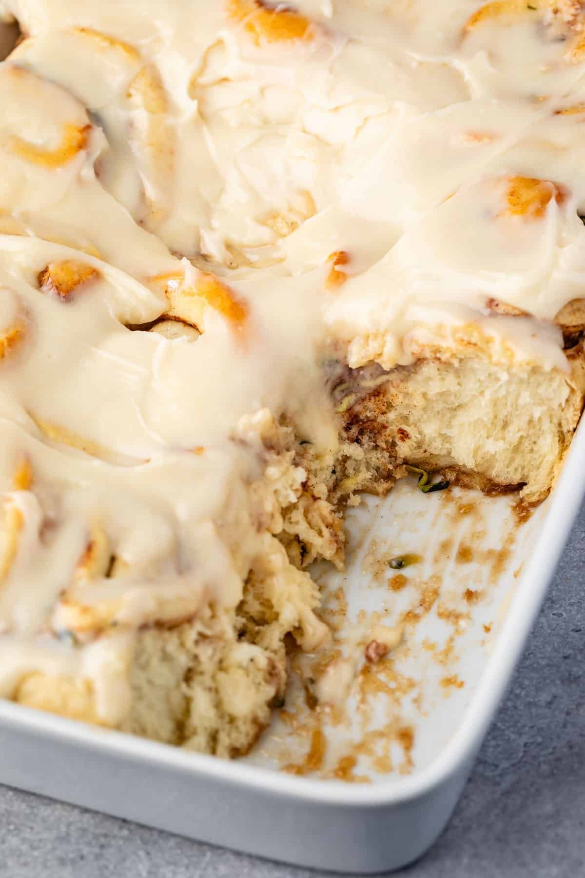 zucchini cinnamon rolls in a white pan covered in frosting.