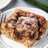 slice of square coffee cake on a white plate with powdered sugar on top.