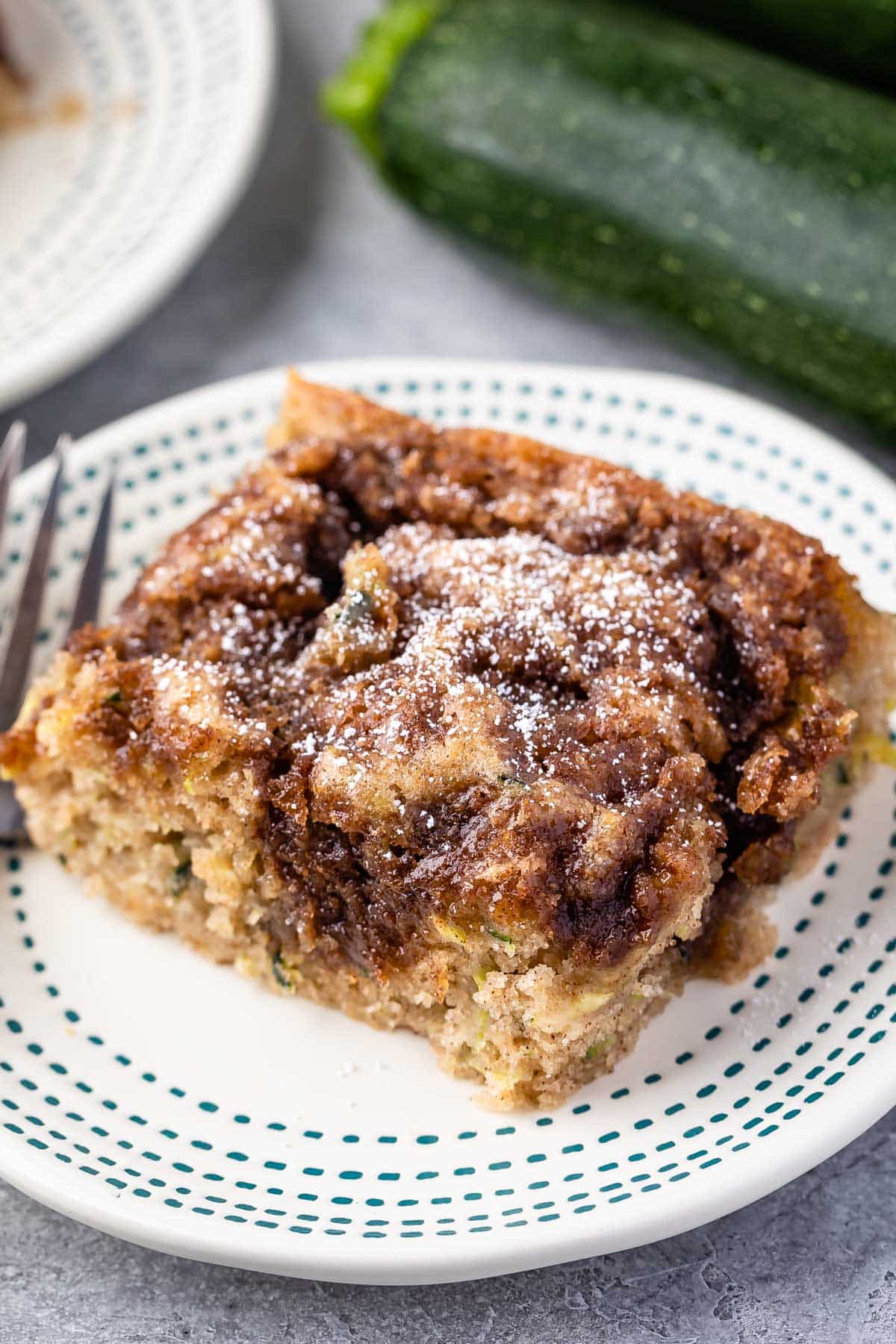 slice of square coffee cake on a white plate with powdered sugar on top.