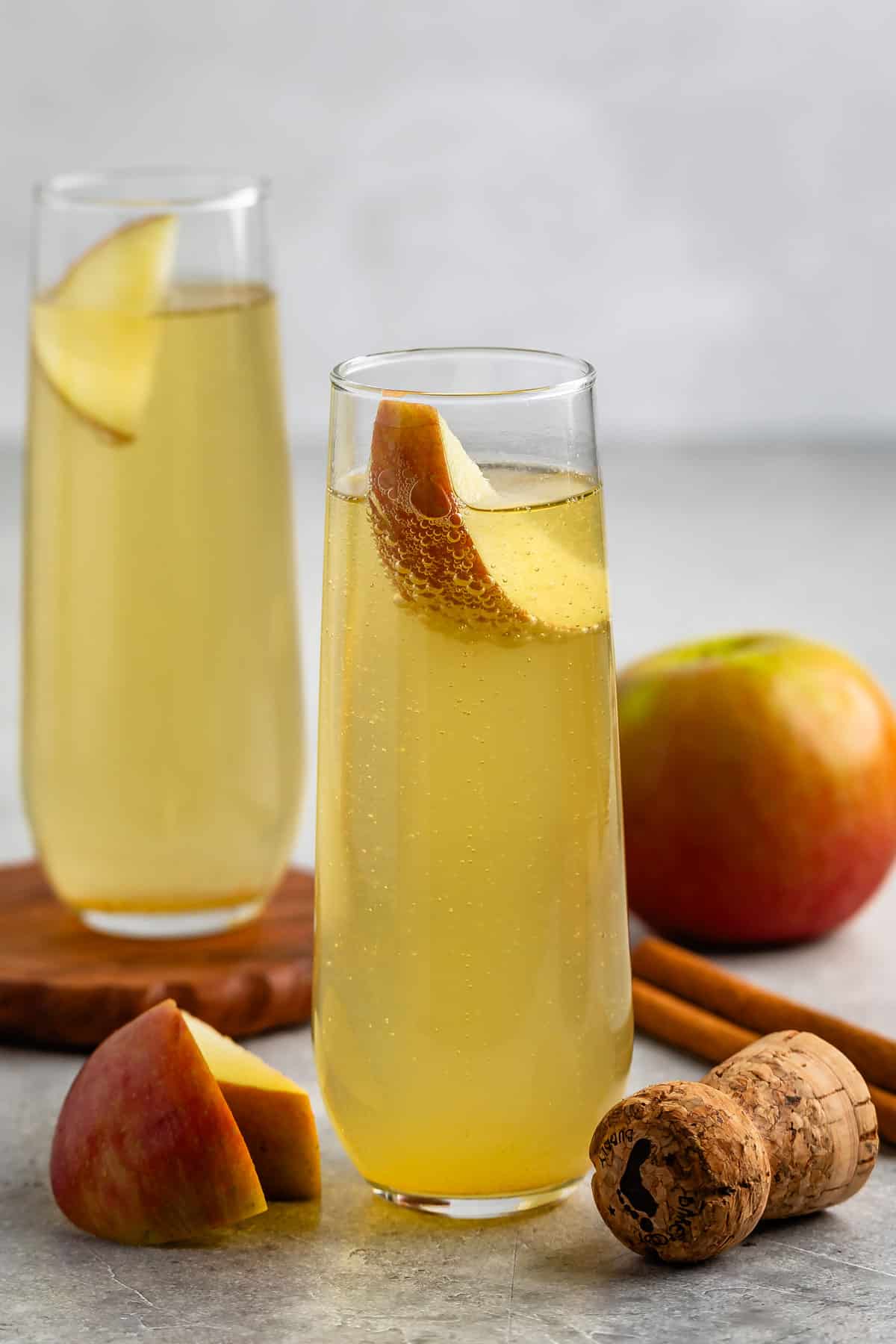 yellow drink in a tall clear glass with an apple slice in the glass.