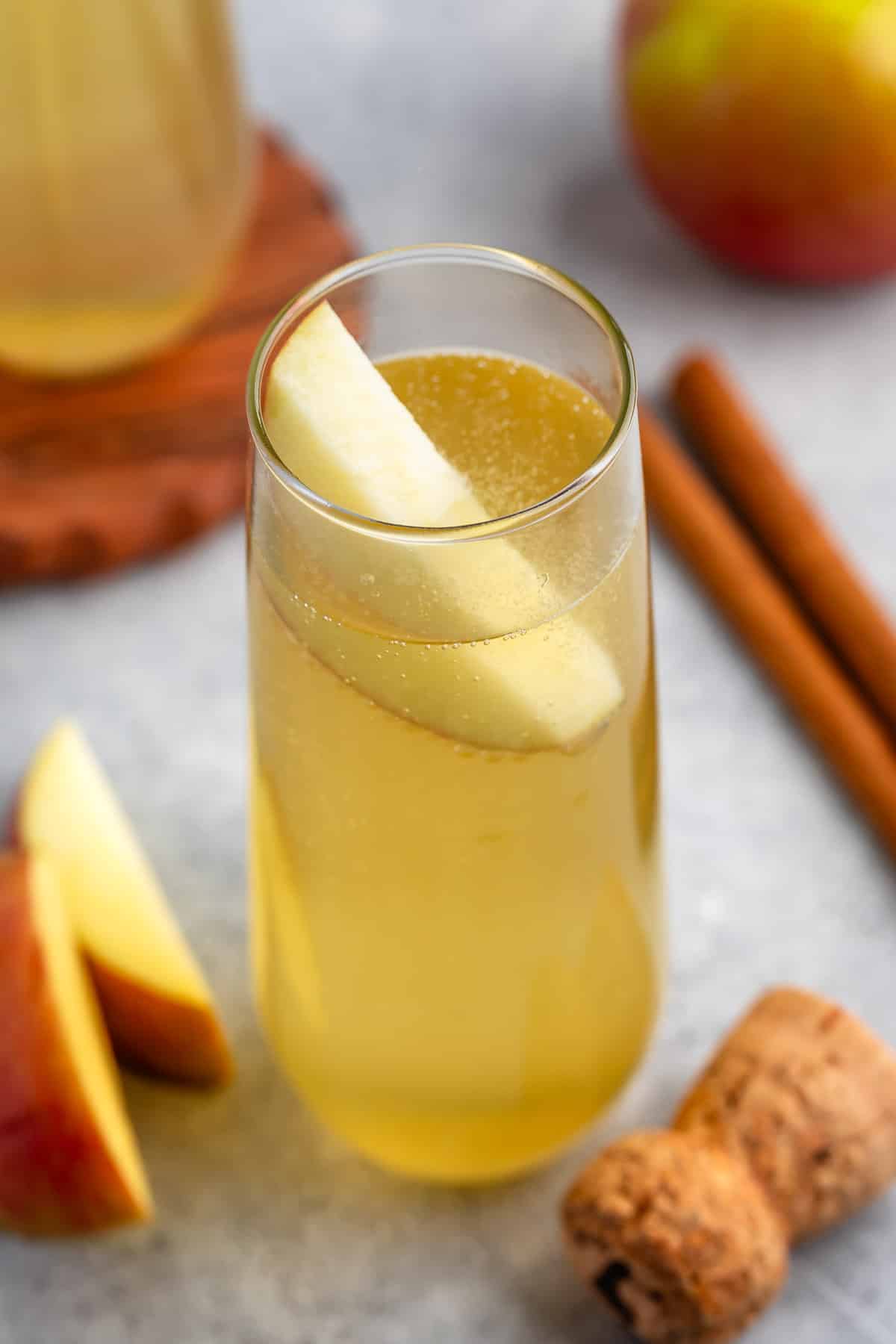 yellow drink in a tall clear glass with an apple slice in the glass.