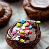 brownie bite on parchment paper with chocolate frosting and colorful sprinkles on top.