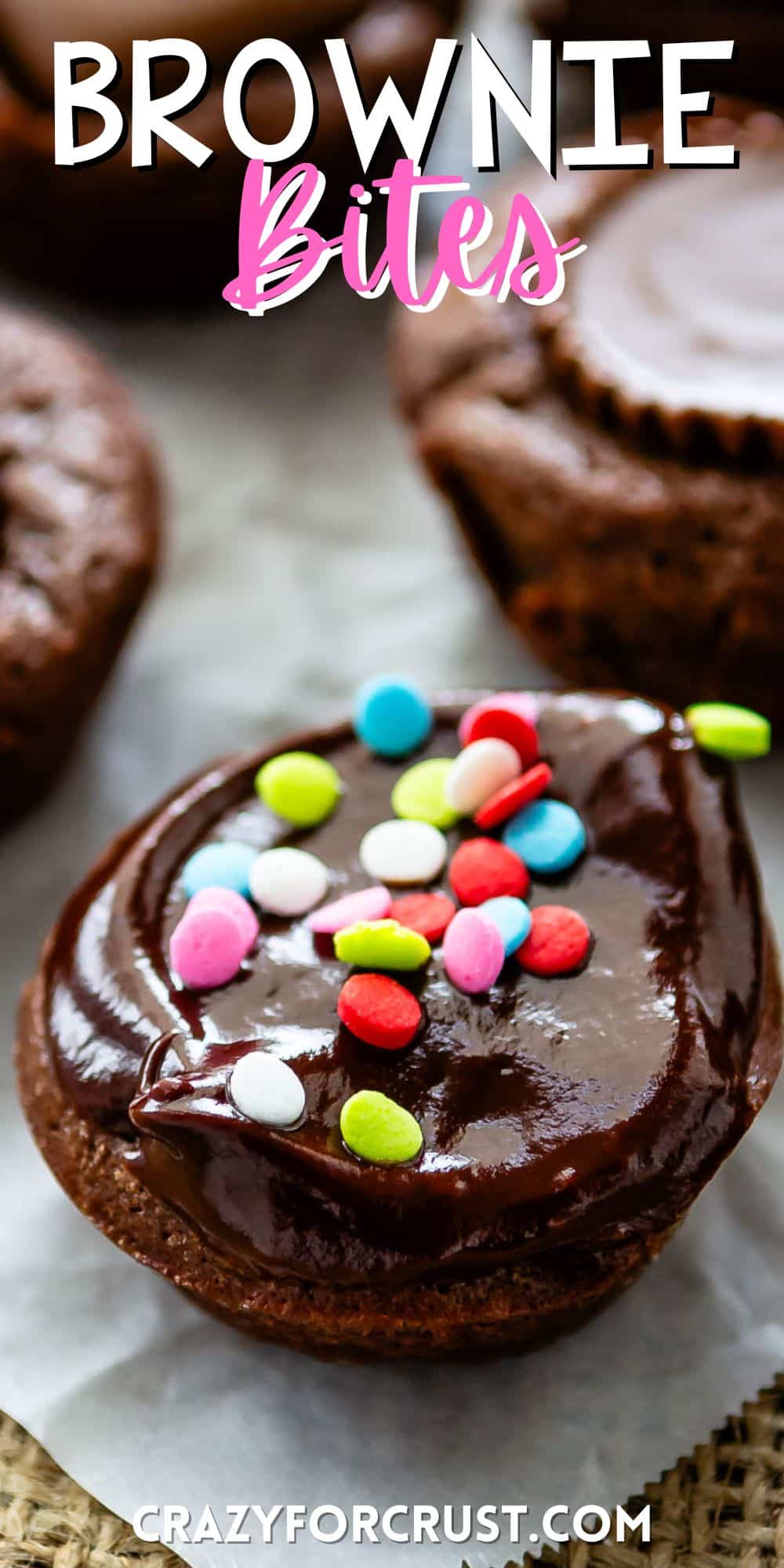 brownie bite on parchment paper with chocolate frosting and colorful sprinkles on top with words on the image.