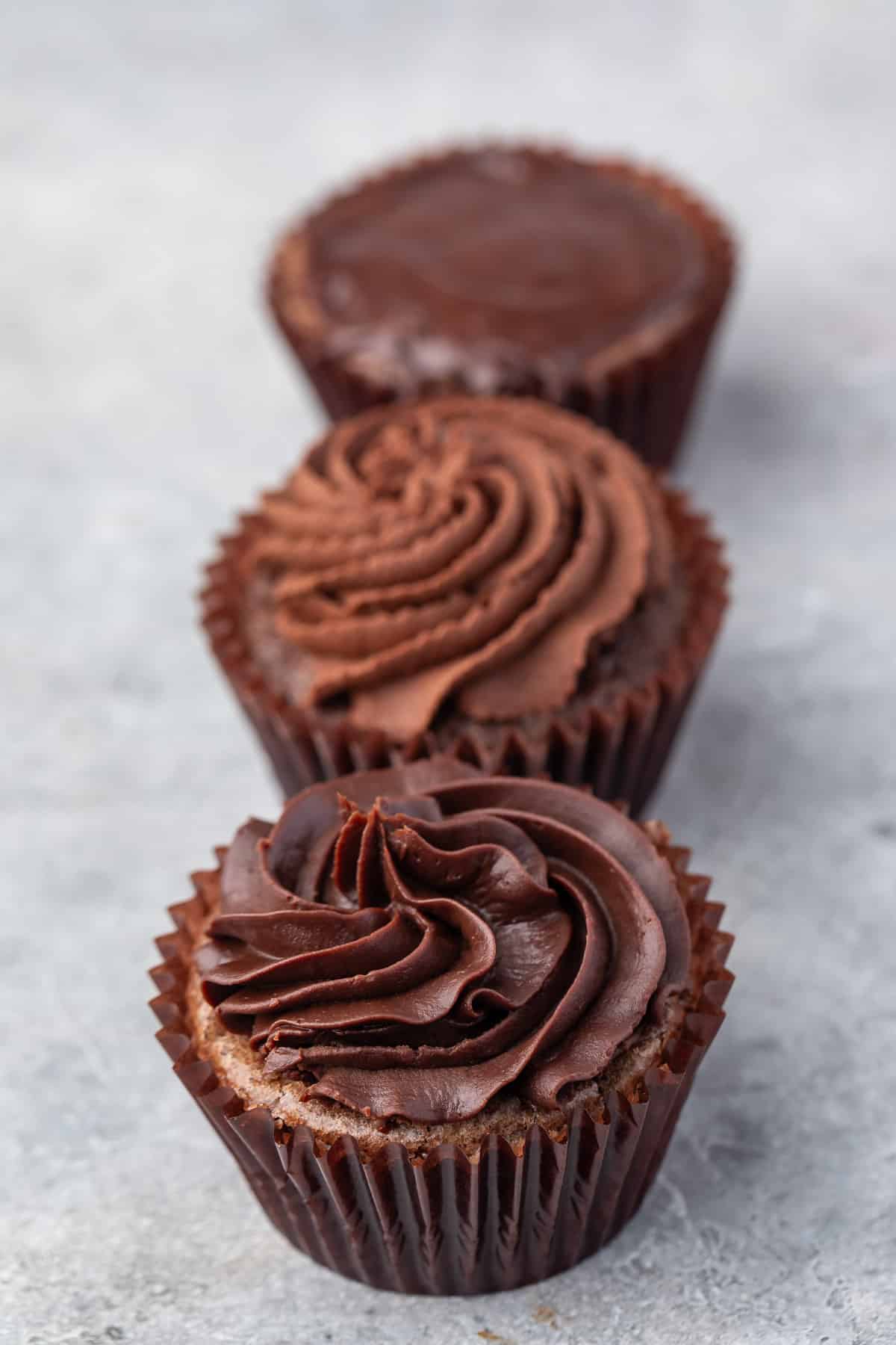 3 chocolate cupcakes with different types of ganache frosting