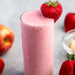 tall clear glass holding light pink smoothie with a strawberry on the rim.