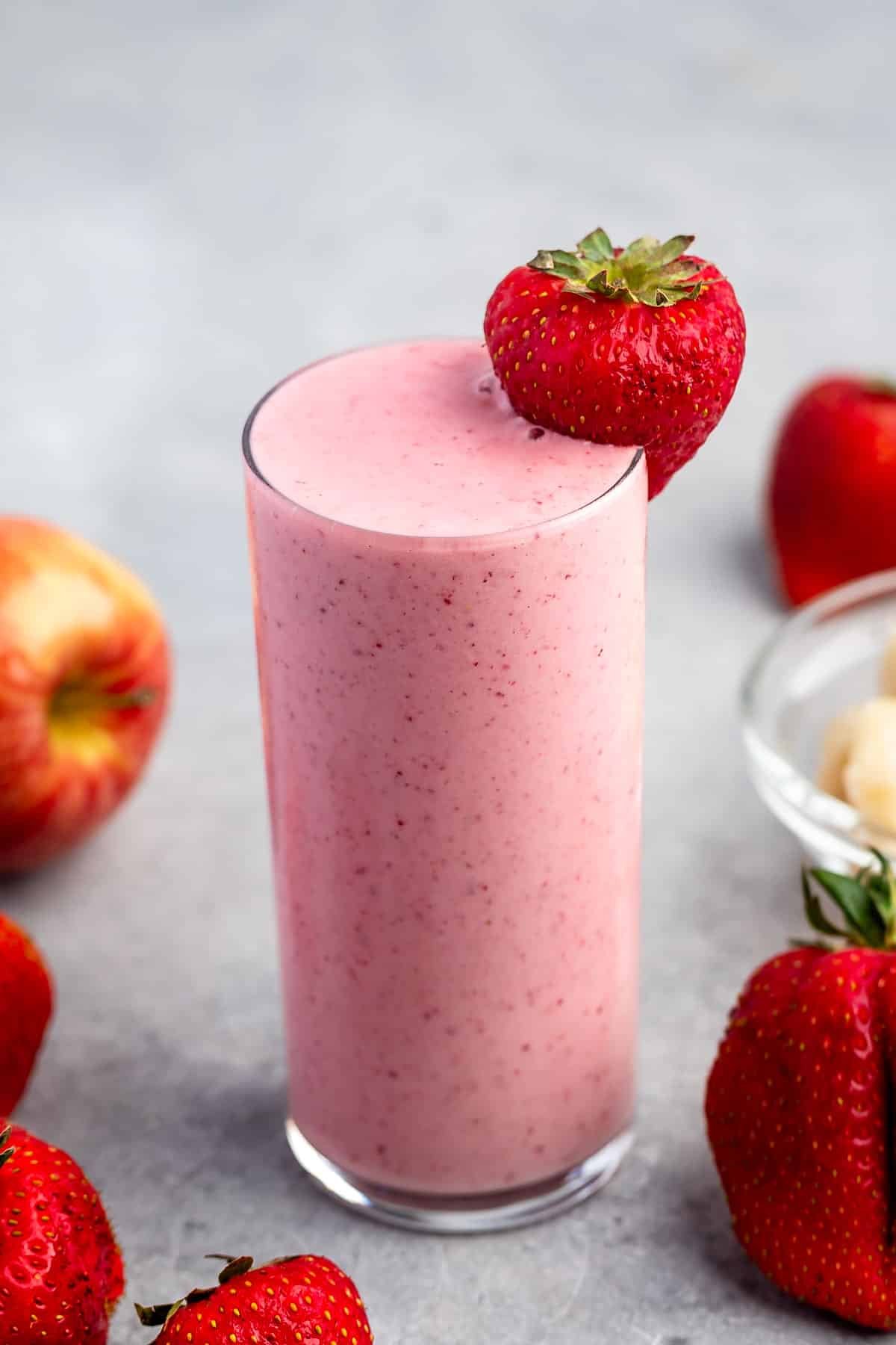 tall clear glass holding light pink smoothie with a strawberry on the rim.