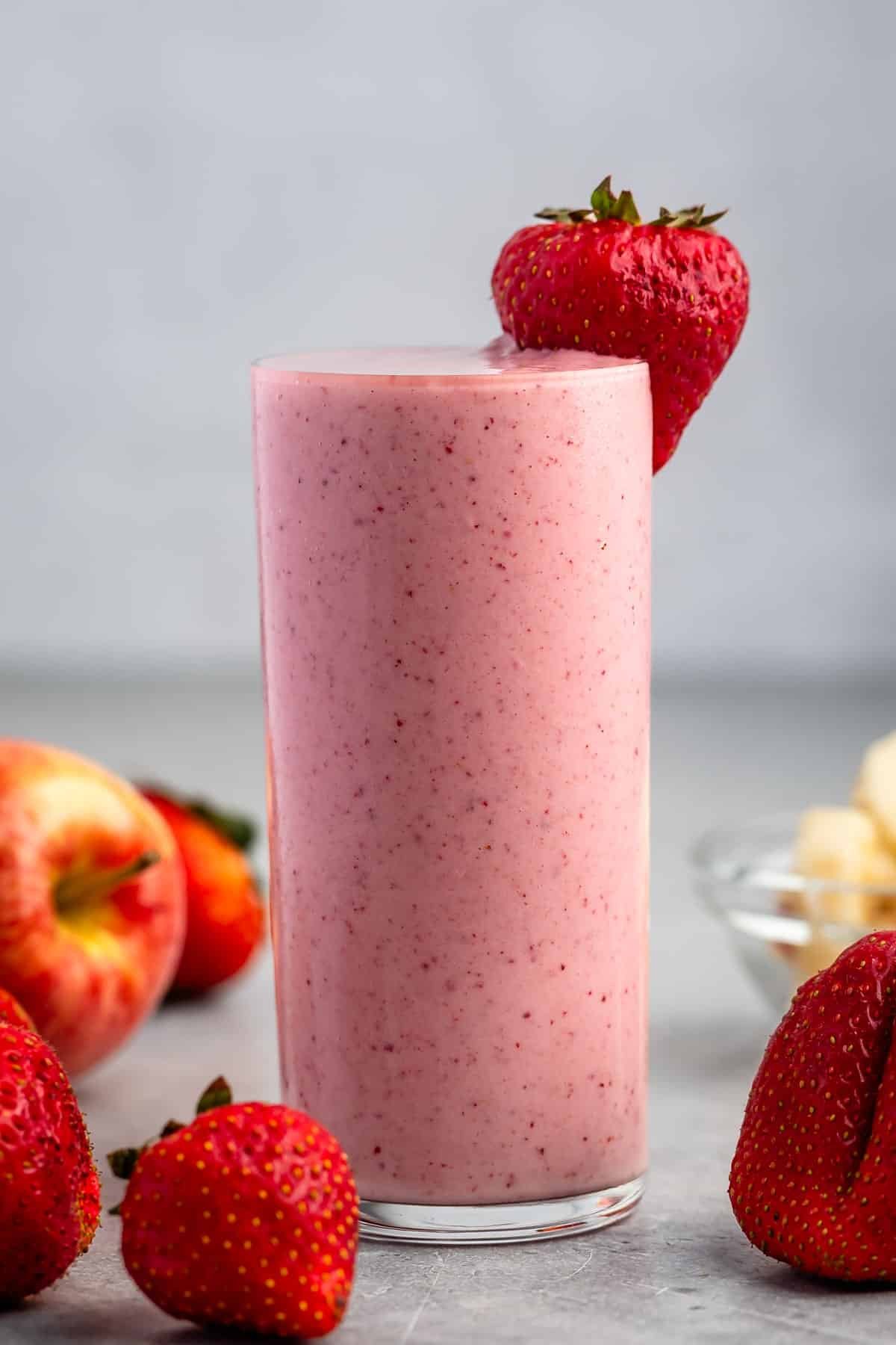 tall clear glass holding light pink smoothie with a strawberry on the rim.
