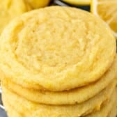 A close-up of a stack of golden-yellow Lemon Pudding Cookies resting on a cooling rack, with a sliced lemon visible in the background.