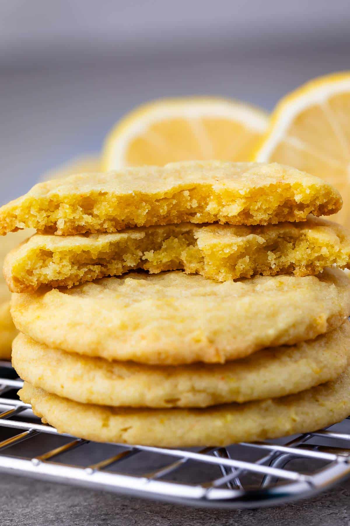stacked lemon cookies with sliced lemons in the background.
