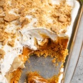 dessert with white cream and graham cracker crumbs on top in a clear pan.