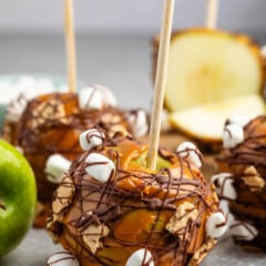 green apple dipped in caramel and chocolate with marshmallows and graham cracker stuck to side.